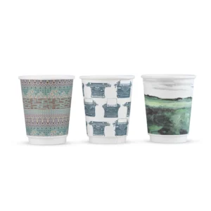 Three white takeaway cups with patterned designs: geometric motifs, typewriters, and a green landscape.