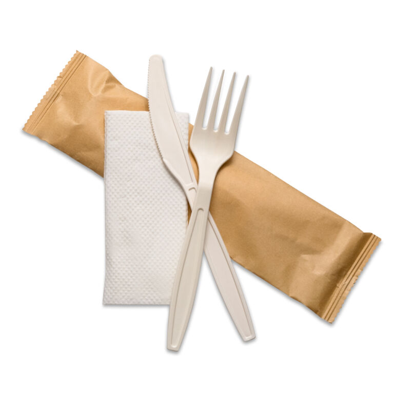 Reusable cornstarch cutlery kit with a knife, fork and white napkin in a sealed brown pouch.