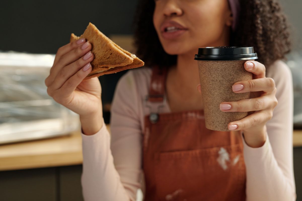 Woman eating sandwich and drinking hot drink in recyclable packaging